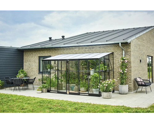 Kas met planten naast een huis met terras en tuinmeubelen