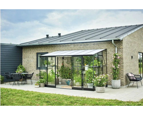 Broeikas met planten en tuinaccessoires op een terras naast een woonhuis