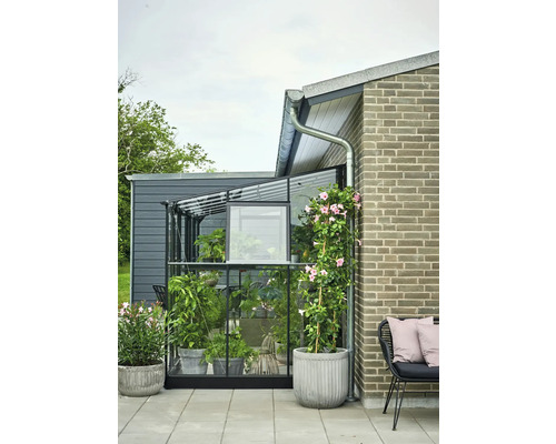 Kas met planten en bloemen in potten op een terras naast een huis.