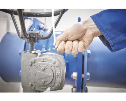 Een arbeider bedient een industriële klep met een moersleutel.