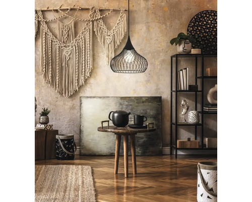Woonkamer met macramé wandkleed, draadlampenkap, kleine tafel met theepot en rek