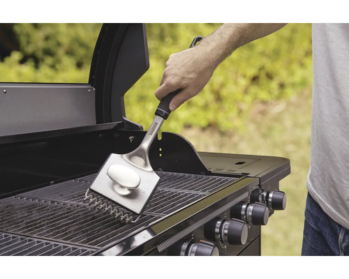 Een persoon maakt het grillrooster schoon met een grillborstel.