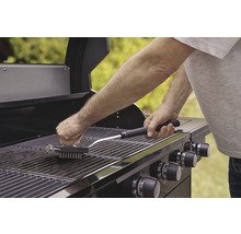Een persoon reinigt een grillrooster met een grillborstel.