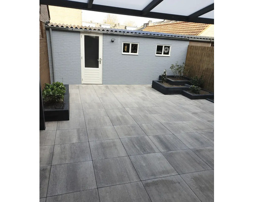 Terras met grijze bestrating, tuinhuis en plantenbakken.