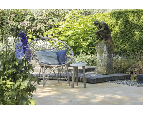 Tuinscene met rotan stoel, bijzettafel en standbeeld