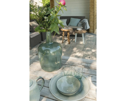 Terras met gedekte tafel, bloemen in een glazen vaas en zithoek op de achtergrond