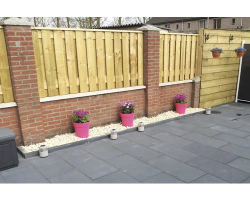 Tuinaanzicht met houten schutting, bestrating en bloemen in potten.