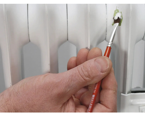 Een hand houdt een penseel vast om een radiator te schilderen.