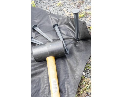 Tuinvlies wordt met een rubberen hamer en grondankers bevestigd.