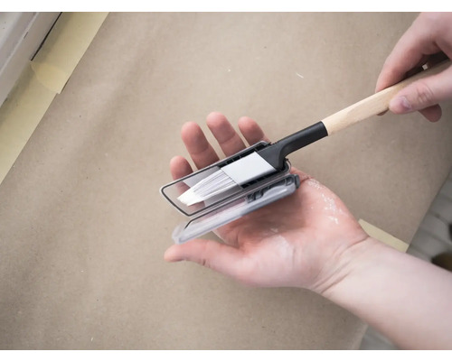 Verfkwast met verfdoos wordt door een hand vastgehouden.